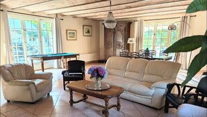 Un salón amplio con mesa de billar, sofás de cuero y una araña.