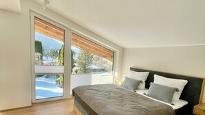 A bedroom with a large bed, wooden flooring, and a view of a snowy landscape through a sliding door. - Modern loft for 6 with mountain views | Bad Ischl (Bad Ischl)