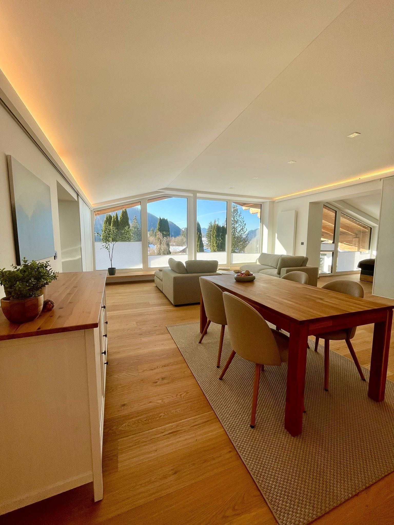 A modern living space with a dining area, sofas, and a large window offering a mountain view.