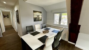 A dining area with a table set for four, surrounded by chairs, a window with a view, and a framed picture on the wall. - Les Etrangers 402 - La Bourboule (La Bourboule)