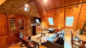 A cozy wooden interior with a stone wall, a television, a fireplace, and a sofa.