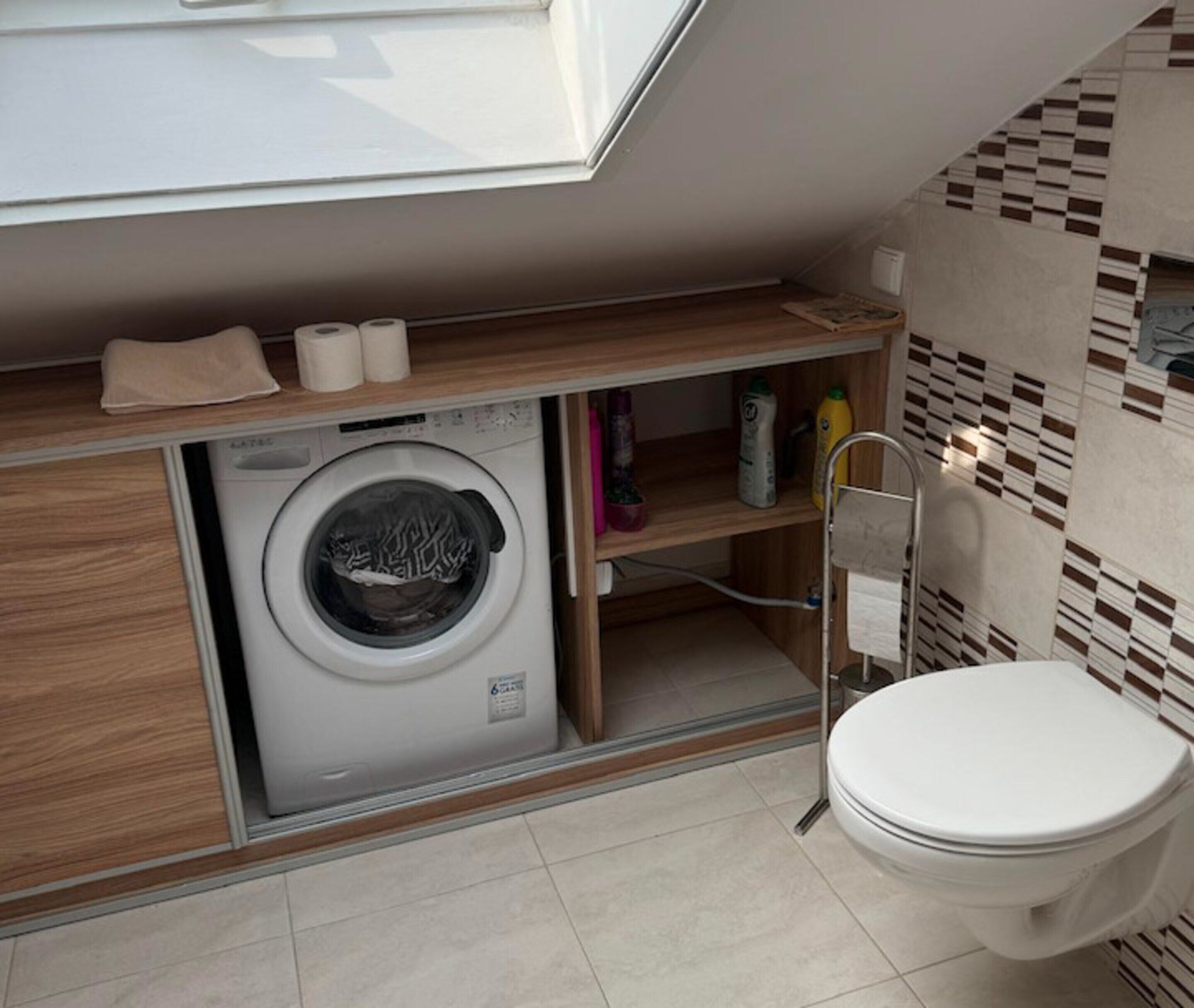Een kleine badkamer met een wasmachine, toilet en een plank met toiletartikelen.