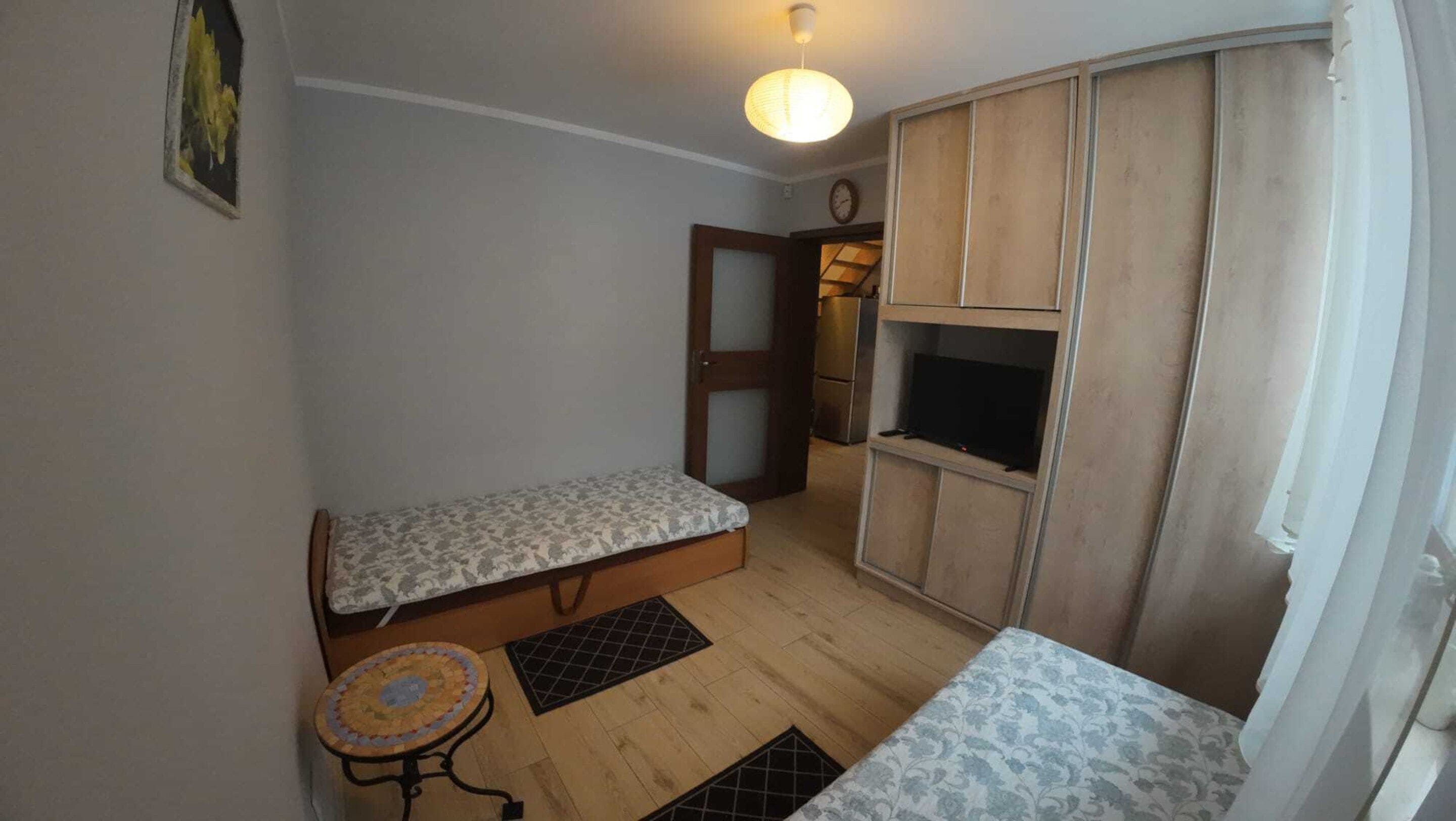 Een kleine kamer met een bed, een tafeltje, een televisie en een kledingkast.