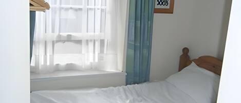 A single bed with white bedding in a room with a window, a wooden headboard, and a framed picture on the wall.
