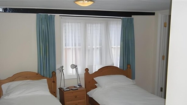 Une chambre à coucher avec deux lits en bois, une table de chevet avec une lampe et une fenêtre avec des rideaux.