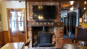 Un pub chaleureux avec une cheminée en briques, des tables en bois et un téléviseur à écran plat fixé au-dessus du foyer.