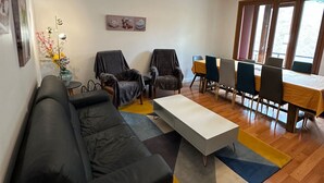 A modern living room with a black sofa, a coffee table, and a dining area with a table and chairs. - Villa Janchrisma - Montdore - 11pers (Mont-Dore)