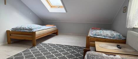 A small attic bedroom with two wooden beds, a skylight, a clock, and a patterned rug.