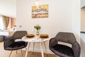 Een eethoek met een marmeren tafel, twee fluwelen stoelen, een vaas met bloemen en een schilderij van een brug aan de muur.