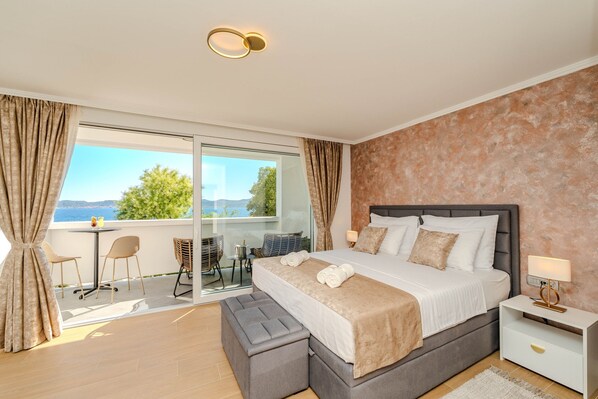 Een slaapkamer met een groot bed, een nachtkastje, een bankje, een tafel met stoelen en uitzicht op de omgeving.