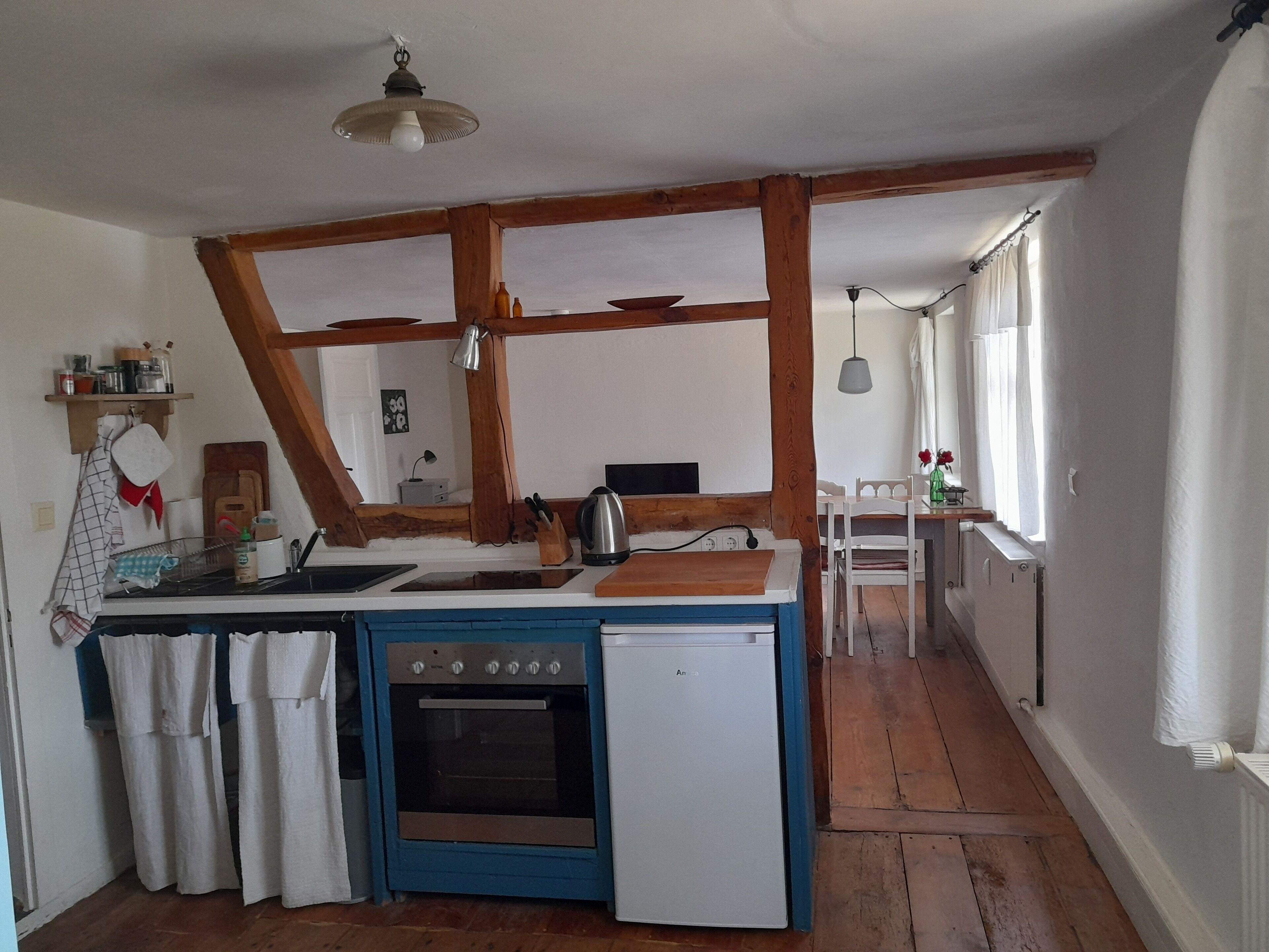 Een compacte keuken met een blauw-witte kleurenschema, houten balken, een kleine oven en een spoelbak.
