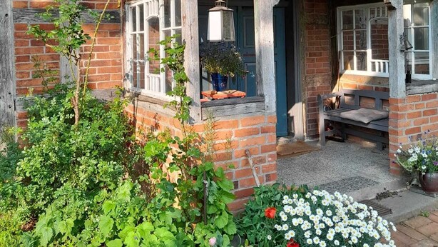 Ein traditionelles Backsteinhaus mit einer Holzveranda, einer Bank und einem Blumentopf.