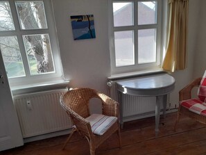 Ein Zimmer mit einem Korbstuhl, einem kleinen Tisch und einer Heizung.