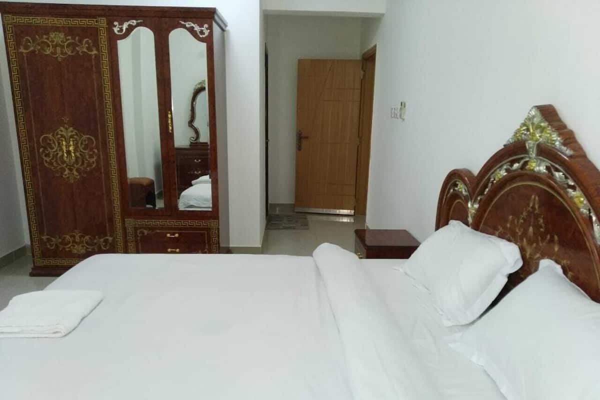 A hotel room with a large bed, a wooden wardrobe, and a mirror.