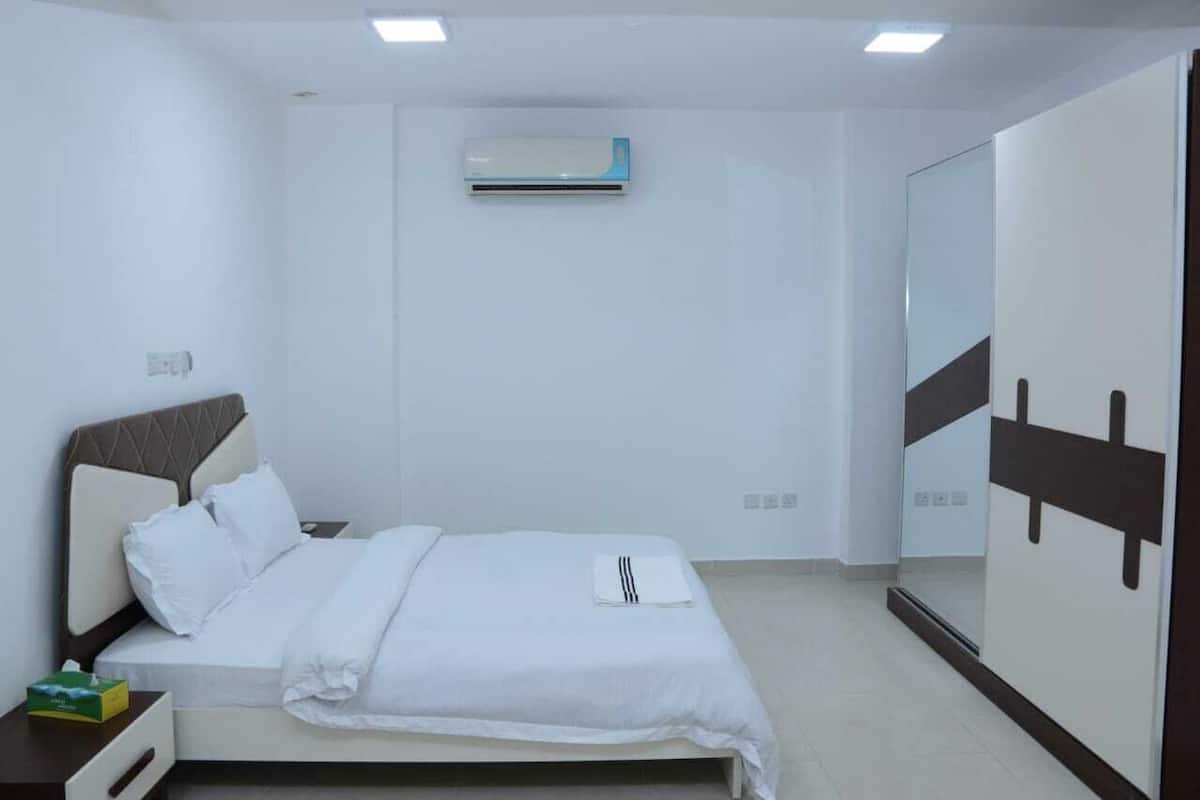 A hotel room with a bed, bedside table, and an air conditioning unit on the wall.