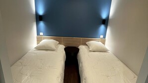 A small, compact room with two single beds, a wooden floor, and a blue accent wall. - L\"ecrin D\"edern Degle Mont Dore deg Ski Degrandonnee deg (Mont-Dore)