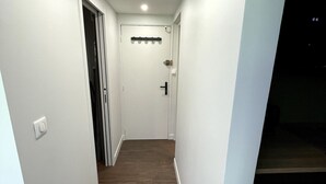 A narrow hallway with white walls and wooden flooring, leading to a door with a coat rack above it. - L\"ecrin D\"edern Degle Mont Dore deg Ski Degrandonnee deg (Mont-Dore)