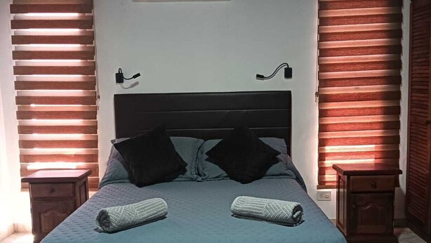 Un dormitorio con cama, dos mesitas de noche, aire acondicionado y persianas de madera.