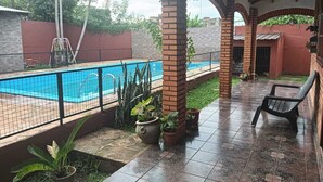 Un patio cubierto con piscina, plantas en macetas y una silla.