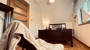 A cozy room with a wooden floor, a dark wooden bed, a small bedside table with a lamp, and a window with curtains. - Holiday Home, Sea, Jacuzzi, for 6 People (Wladyslawowo)
