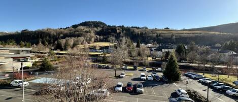 A parking lot with multiple cars, a building with a modern design, and a hilly landscape in the background.