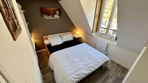 A bedroom with a bed, bedside tables, a radiator, and a window with a view of the outside. - Practical Apartment in La Bourboule (La Bourboule)