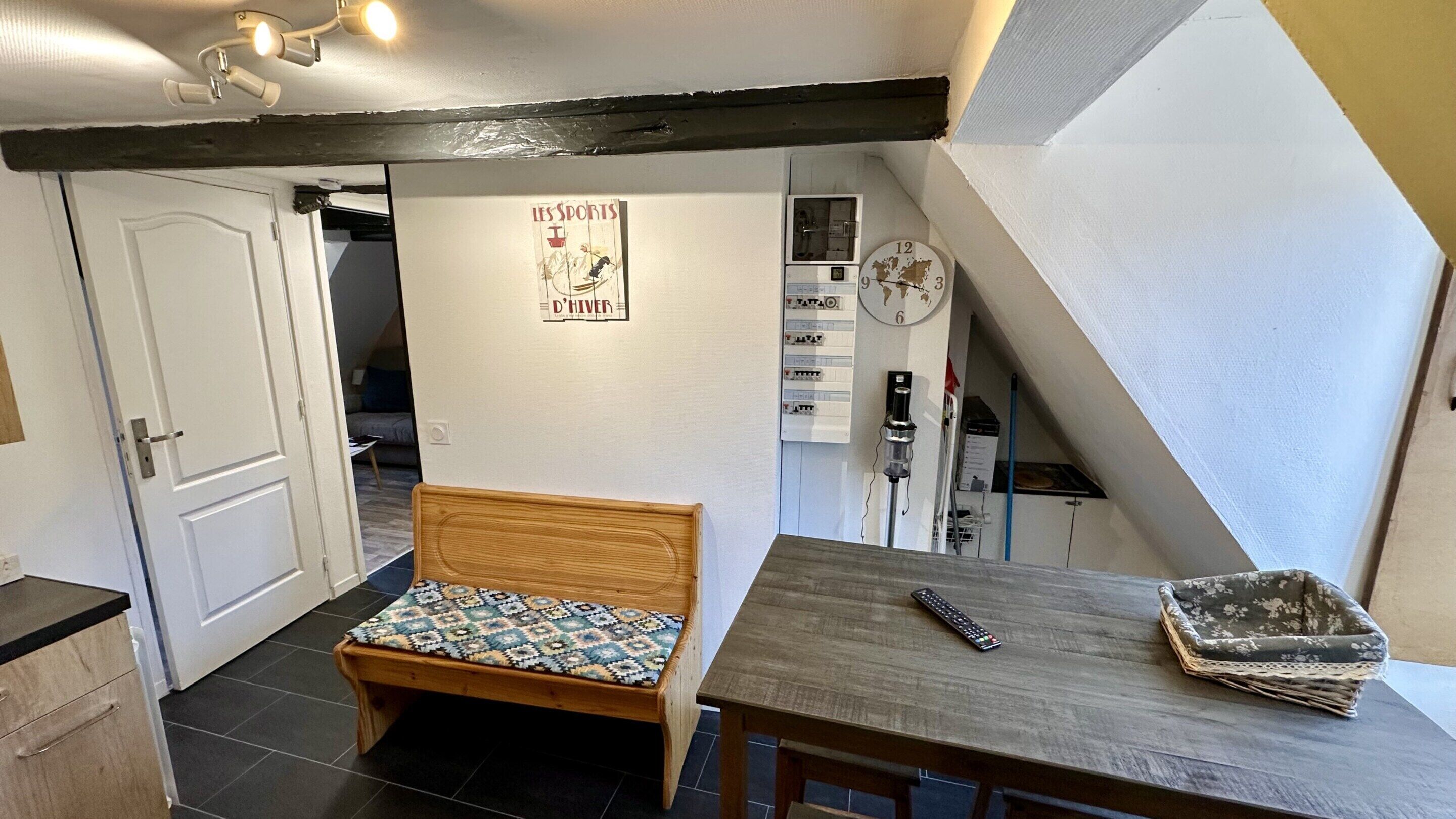 A small room with a wooden bench, a table, a wall clock, and a poster.