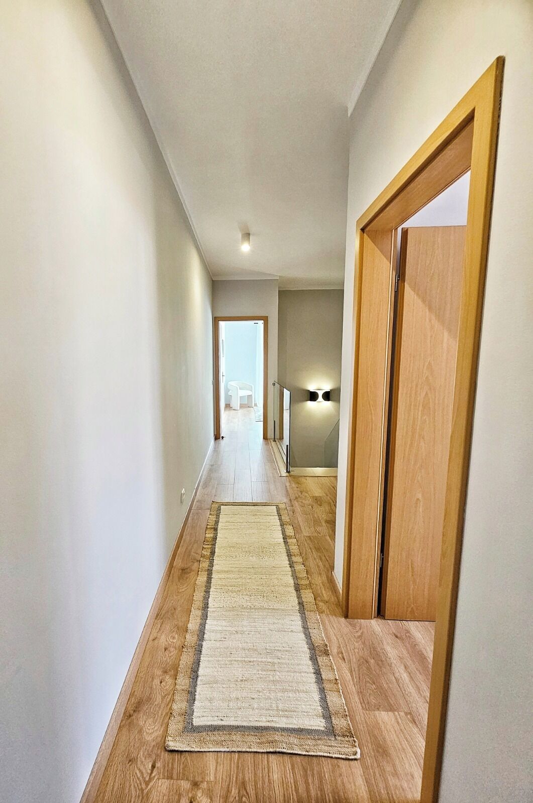 A hallway with wooden flooring, a rug, and a door on the right.