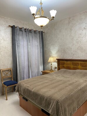 A bedroom with a large bed, a wooden headboard, a nightstand with a lamp, a chair, and a chandelier. - Marbella Real Apartment (Marbella)