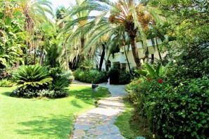Un sendero en un jardín que lleva a un edificio con fachada blanca y arcos.
