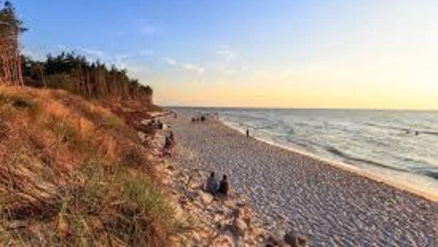 A beach with a rocky shoreline, people sitting on the sand, and a clear sky. - Holiday Home, 4 Bedrooms, Private Garden (Ustka)