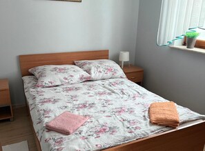 A neatly made bed with floral bedding, a wooden headboard, and a nightstand with a lamp. - Holiday Home, 4 Bedrooms, Private Garden (Ustka)