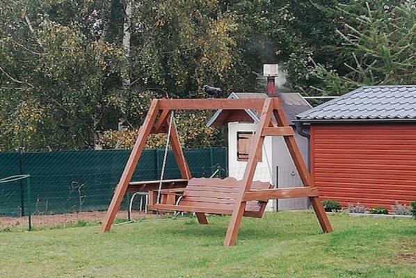 A wooden swing set in a grassy yard with a red building in the background. - Holiday Home, 4 Bedrooms, Private Garden (Ustka)