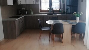 A modern kitchen with wooden cabinets, a central island with chairs, a window with curtains, and a refrigerator. - Holiday Home, 4 Bedrooms, Private Garden (Ustka)