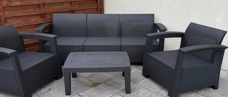 A set of outdoor wicker furniture consisting of a sofa, two armchairs, and a small table.