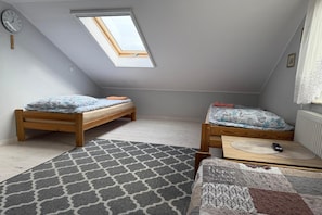 A small attic bedroom with two wooden beds, a skylight, a clock, and a patterned rug. - Holiday Home, 4 Bedrooms, Private Garden (Ustka)