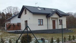 A two-story house with a sloped roof, a fenced yard, and a small garden area. - Holiday Home, 4 Bedrooms, Private Garden (Ustka)