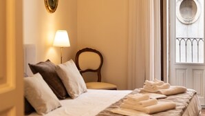 A neatly made bed with pillows, a bedside lamp, and a window with curtains. - Ferrari Mansion • Historic Noble Residence by the Cathedral (Catania)