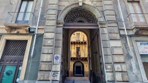 A historic building with a central archway, multiple balconies, and a sign indicating a business. - Ferrari Mansion • Historic Noble Residence by the Cathedral (Catania)