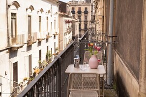 A balcony with a table, a chair, a vase with flowers, and a railing. - Ferrari Mansion • Historic Noble Residence by the Cathedral (Catania)