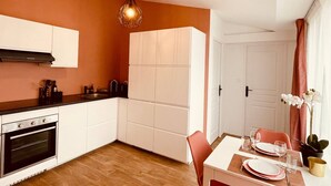 Uma cozinha compacta com armários brancos, forno embutido e um espaço de jantar com mesa posta para dois.