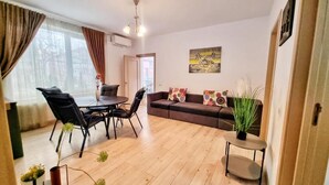 A living room with a wooden floor, a sofa, a dining table with chairs, and a painting on the wall.