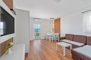 Un soggiorno moderno con televisore a schermo piatto, un divano marrone, un tavolo da pranzo bianco e un balcone con vista.