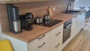 Eine moderne Küche mit Holztischplatte, Edelstahlgeräten, einer schwarzen Kaffeemaschine und einem gelben Stuhl.