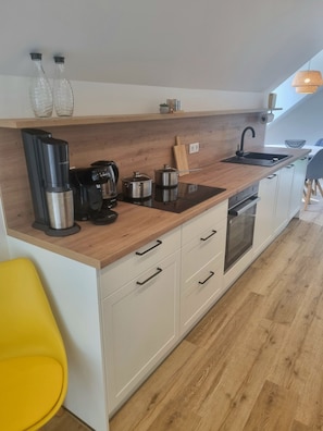 A modern kitchen with a wooden countertop, stainless steel appliances, a black coffee maker, and a yellow chair. - Mindful Living vacation apartment on the Lower Rhine - to relax in nature (Hamminkeln)