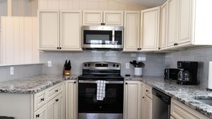 A kitchen with light-colored cabinets, a stainless steel stove, a microwave, and a coffee maker.