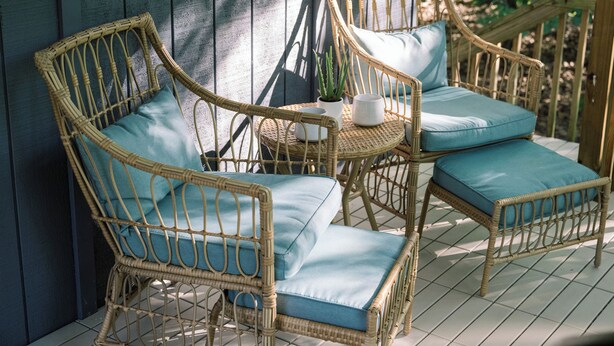 Wicker chairs with blue cushions and a small table with a potted plant on a porch.