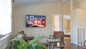 A living room with a large TV, a sofa, a coffee table, and a potted plant.