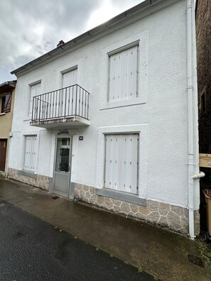 A two-story building with a white exterior, a balcony with metal railings, and a stone base. - Centrally Located Villa in Mont-dore (La Bourboule)