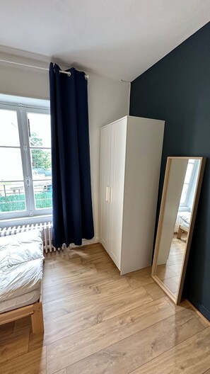 A bedroom with a bed, a wardrobe, a mirror, and a window with curtains. - Centrally Located Villa in Mont-dore (La Bourboule)